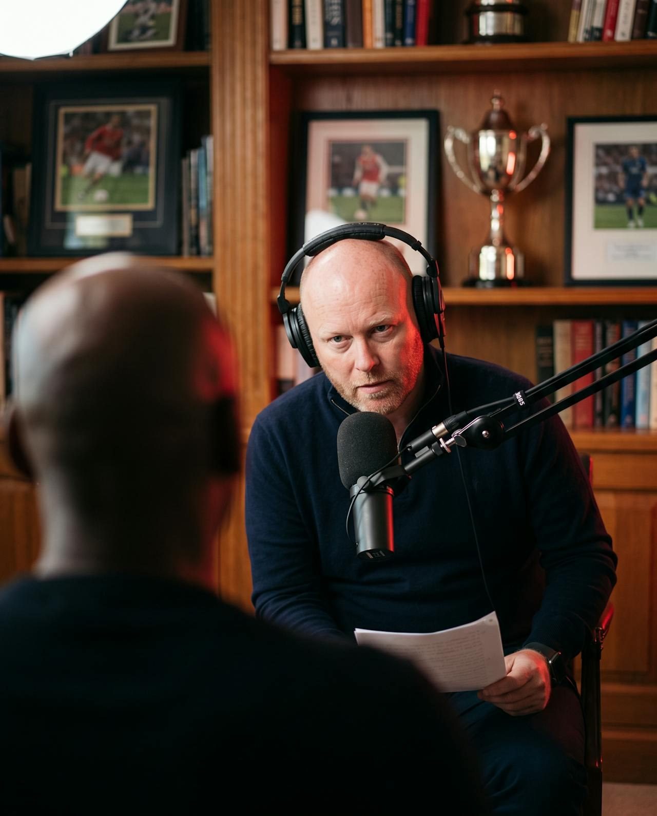 Dan interviewing a guest in a study lined with sporting memorabilia